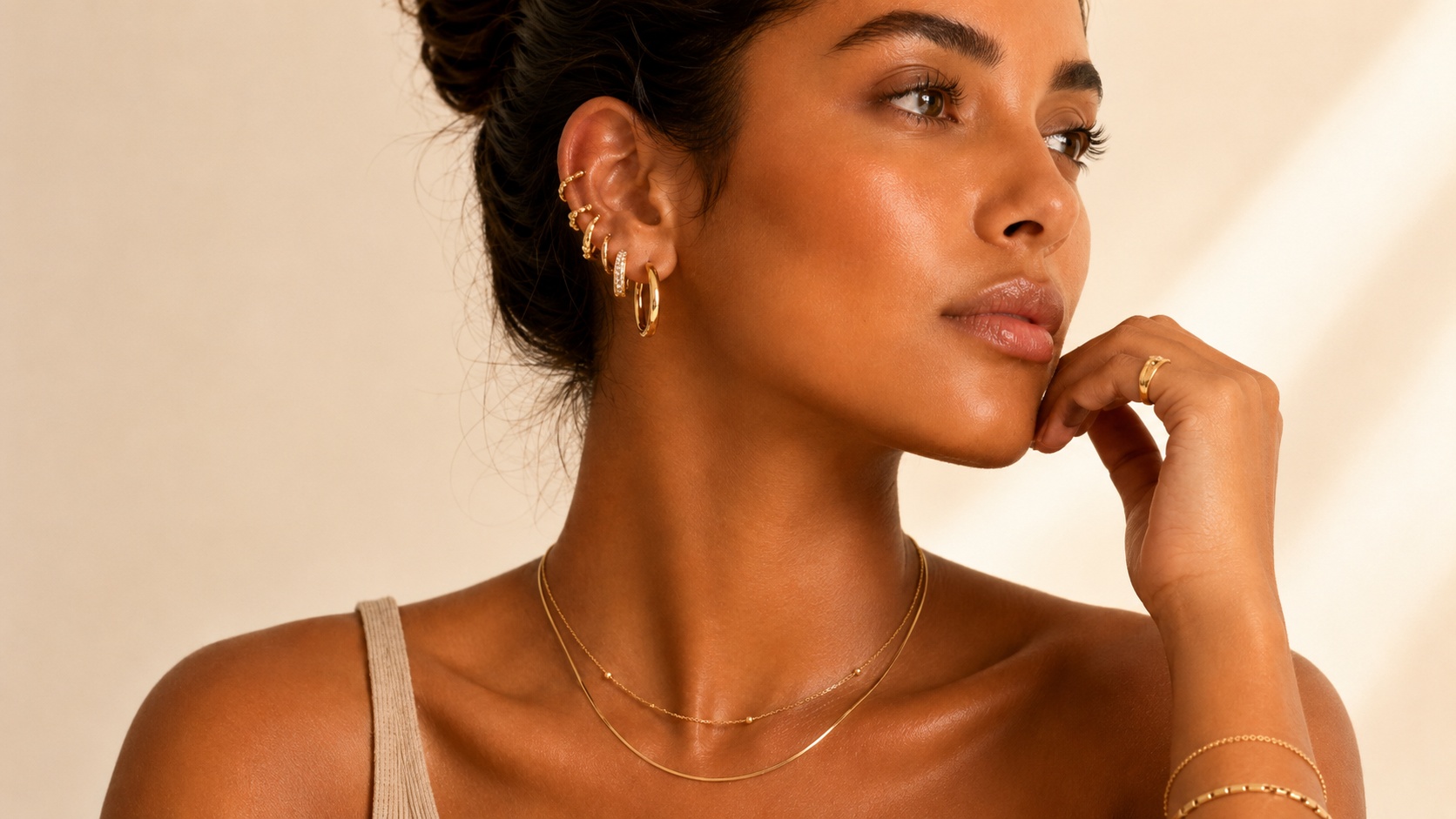 Model wearing layered gold-plated earrings, necklace, bracelet, and ring